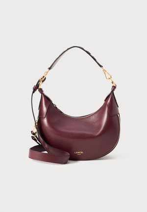 Sac à main en cuir violet foncé en forme de croissant avec fermeture éclair dorée, bandoulière amovible et logo doré "LANCEL PARIS" à l'avant.