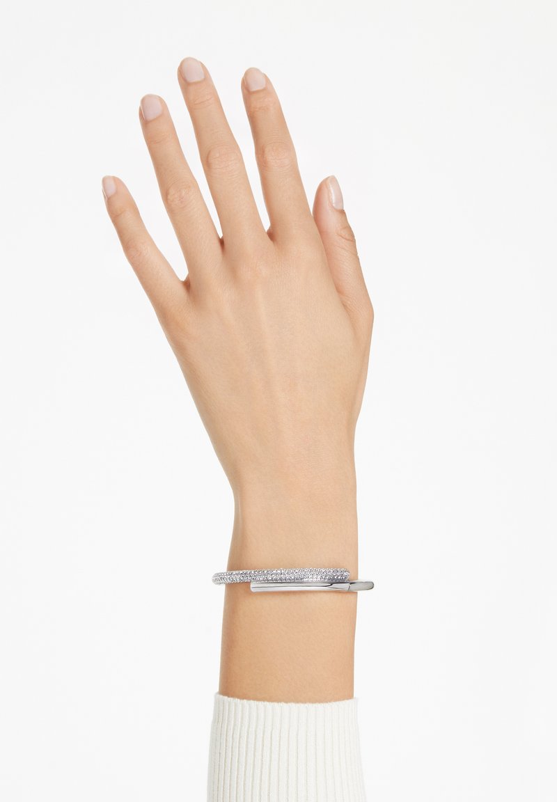 Bracelet en métal avec une surface texturée, doté d'une barre d'accent lisse en argent. Porté sur une main avec des ongles de couleur neutre.