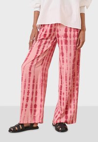 Wide-leg pants in a lightweight fabric, featuring a pink base with red tie-dye stripes. Worn with black sandals.
