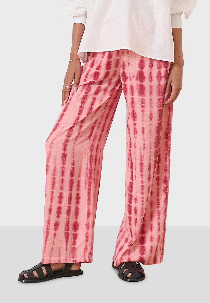 Wide-leg pants in a lightweight fabric, featuring a pink base with red tie-dye stripes. Worn with black sandals.