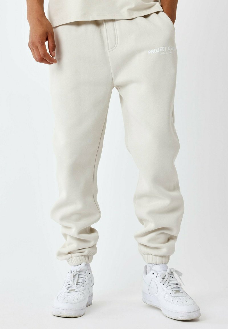 Pantalones de chándal de color claro, ajustados en el tobillo, con puños acanalados y una cintura elástica. Presenta el texto "PROJECT X" en blanco en la parte frontal.