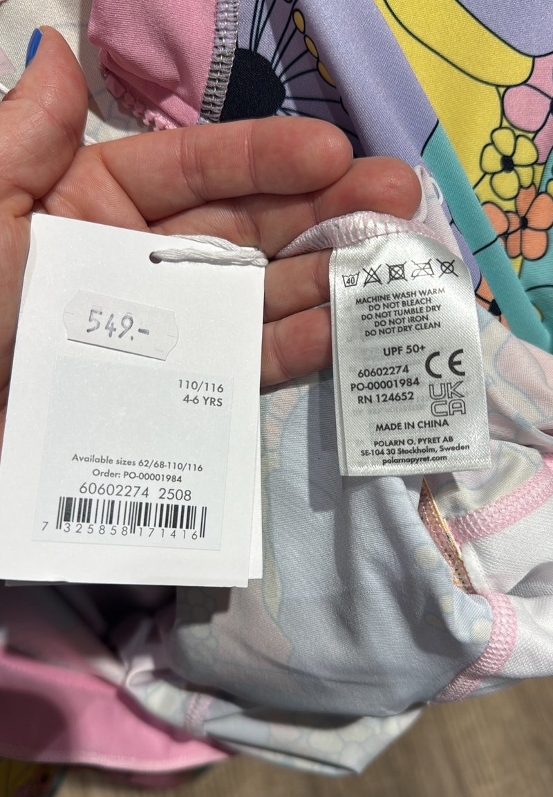 Maillots de bain pour enfants avec un motif floral multicolore, des accents roses et une étiquette indiquant le prix, la taille et les instructions d'entretien.
