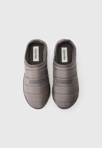 Szürke slip-on cipők, steppelt textúrával, párnázott kialakítással és gumitalppal. Márkázás látható az oldalon és belül.