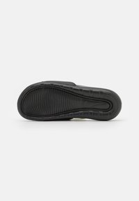 Semelle noire de sneaker avec des motifs texturés et des rainures pour l'adhérence, de forme arrondie et avec un logo Nike discret.