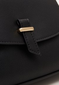 Czarna skórzana torebka o fakturowanej powierzchni, z złotym metalowym zapięciem, zamknięciem na klapę oraz przeszyciami wzdłuż krawędzi.