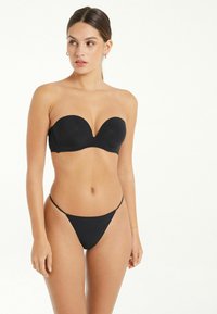 Černý bikinový top bez ramínek s hlubokým výstřihem, doplněný o minimalistické černé tangá kalhotky. Hladká tkanina, elegantní design a žádné viditelné kovové doplňky.