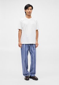 Λευκό κοντομάνικο μπλουζάκι; μπλε ριγέ φαρδιά παντελόνια; λεία υφή; ελάχιστη λεπτομέρεια τσέπης; συνδυασμένο με σκούρες καφέ παπούτσια.