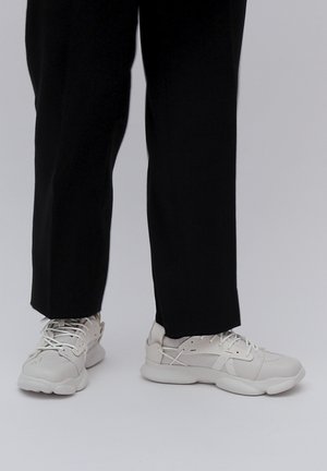 Jasnoszare sneakersy z fakturowaną cholewką, sznurowanym zapięciem i wyściełaną podeszwą, w zestawie z czarnymi spodniami o prostym kroju.