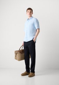 Light blue short-sleeve linen shirt, dark trousers, tan shoes, and a beige duffel bag with brown accents. Simple design and relaxed fit.