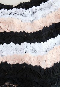 Nauha kantti mustissa, valkoisissa ja ihonvärisissä vaihtoehdoissa esittelee monimutkaisia kukkakuvioita, joissa on aaltoilevat reunat ja hienovarainen rakenne.