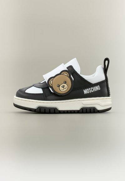 Μαύρο και άσπρο παιδικό αθλητικό παπούτσι Moschino με αυτοκόλλητο λουράκι που έχει πρόσωπο αρκούδου και χοντρή λευκή σόλα.