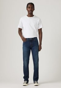 Camiseta blanca de manga corta, jeans de mezclilla azul y zapatillas negras; colores sólidos con un diseño clásico de pierna recta y un ligero desvanecimiento en los jeans.