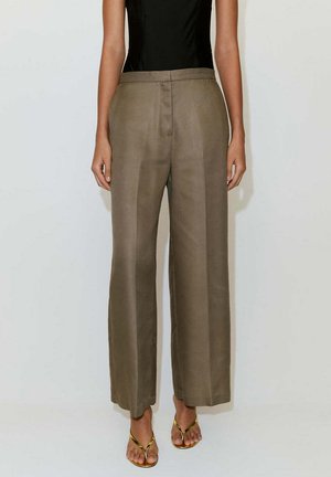 Mujer vistiendo pantalones taupe de talle alto y pierna ancha, combinados con una camiseta negra sin mangas y sandalias doradas tipo tanga.