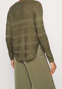 Olivgrüner Strickpullover mit horizontalen, strukturierten Streifen, einem Rundhalsausschnitt und einem etwas längeren Rückenbund, kombiniert mit passenden Hosen.