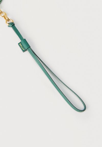 Πράσινο δερμάτινο λουρί καρπού με χρυσή πόρπη και ετικέτα με το λογότυπο Bally, σχεδιασμένο να προσαρτάται σε μια τσάντα ή αξεσουάρ για μεταφορά.