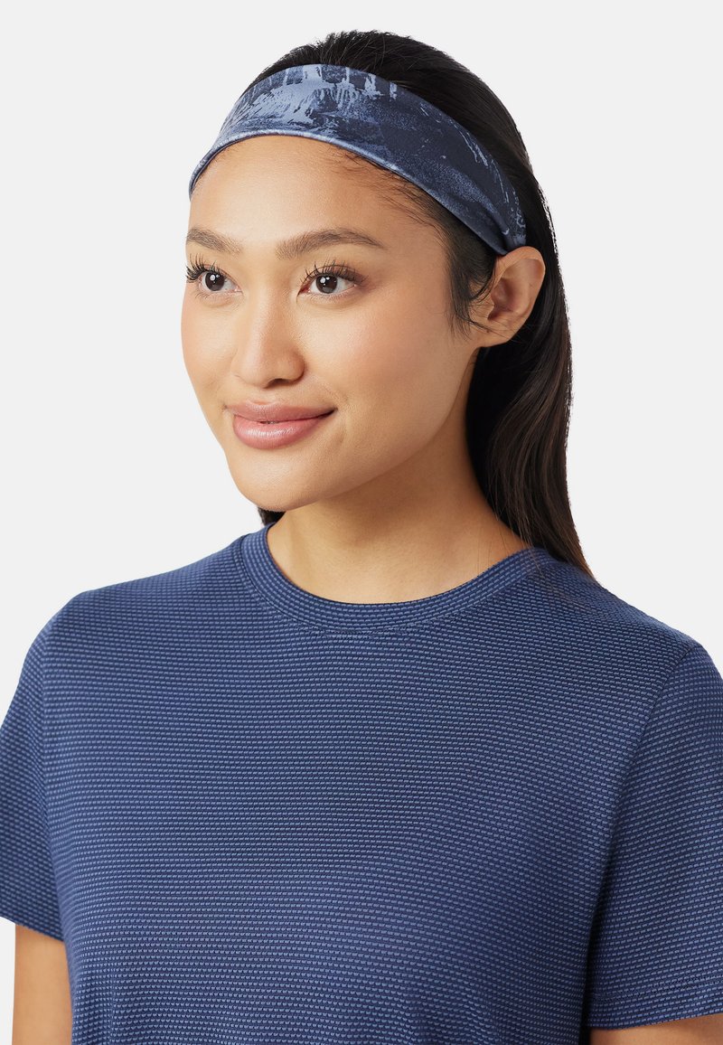 Diadema azul marino hecha de un tejido suave con una textura lisa; presenta un patrón sutil. Combinada con una camisa azul texturizada.