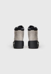 Par de botas de tobillo grises con cuellos acolchados negros y gruesos tacones de plataforma negros, vistas desde atrás sobre un fondo blanco.