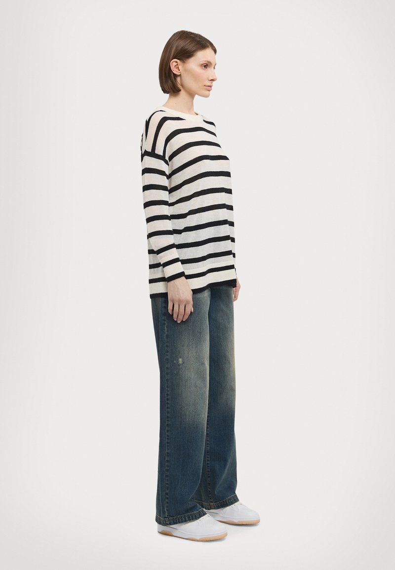 Pull rayé crème et noir, associé à un jean bleu à jambes larges. La tenue est complétée par des baskets blanches, offrant un look décontracté.