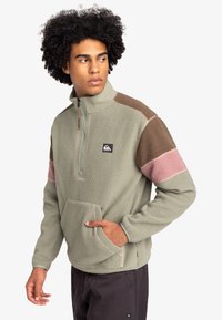 Fleece pullover with a quarter zip, featuring green, brown, and pink color blocking, a front pocket, and a soft, textured exterior.