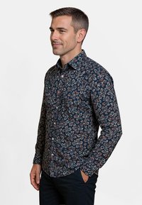 Langarmshirt met een marineblauwe achtergrond en een kleurrijk bloemenpatroon. Gemaakt van stof met een soepele textuur en een knoopsluiting op de kraag.