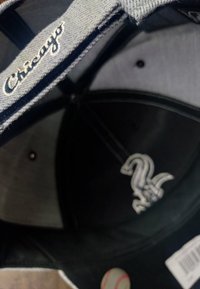 Czarny czapka baseballowa z szarym spodem, haftowym napisem "Chicago" wewnątrz oraz białym logo "Sox" na czubku.