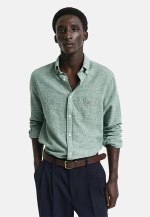 Green textured button-up shirt with a chest pocket, paired with dark trousers and a brown belt. Fabric has a soft, casual appearance.