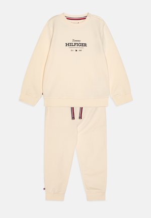Set di felpa e pantaloni color crema realizzato in un tessuto morbido. La felpa presenta un collo tondo e un logo; i pantaloni hanno lacci a righe.