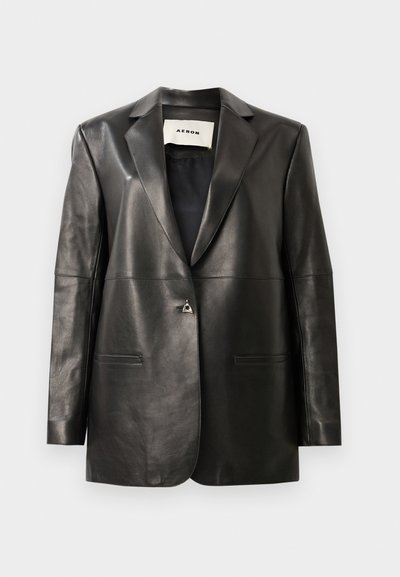 Mustast nahkblazer, millel on kohandatud lõige, sälguga krae, kaks esist pocketit ja üks metallist nööp sulgemiseks. Sile tekstuur.