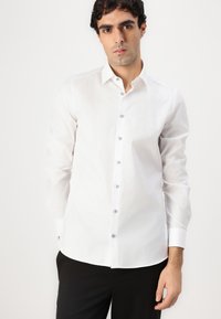 White dress shirt with long sleeves, button-down collar, blue buttons, and a textured fabric. Tailored fit, curved hemline.