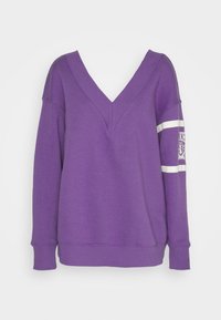 Lila sweatshirt med V-ringning, långa ärmar och ribbade manschetter. Har ett vitt band på vänster ärm och en logopatch på bröstet.