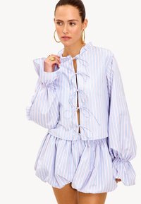 Haut à manches courtes rayé bleu et blanc avec encolure à volants, manches bouffantes et détail lacé à l'avant, associé à une jupe ample.
