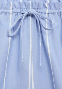 Tissu bleu clair avec des rayures verticales blanches, doté d'une taille froncée et d'un nœud sur le devant pour un ajustement réglable.