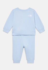Lys blå, myk to-delt antrekk med langermet genser med rund hals og matchende bukser, med en liten hvit logo på genseren.