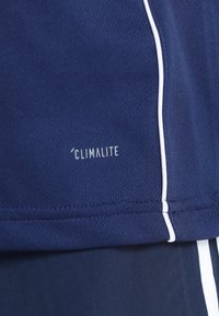 Marinblå atletisk tyg med vit kontrastsöm; pryds av "CLIMALITE"-logotypen i vitt, vilket framhäver fukttransporterande teknologi.