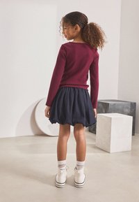 Maroon ribbed long-sleeve top paired with a navy puff skirt. White high-top shoes with black stripes and ankle socks. Simple, clean design.