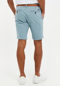 Lyseblå bomulds shorts med flad front og baglommer, brun fletbælt, og opfoldede nederkanter. Båret med hvide sneakers.