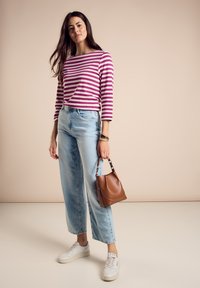 Maglietta a maniche lunghe a righe in rosa e bianco, jeans a gamba larga azzurri, sneakers bianche e una borsa marrone con una silhouette curvata.