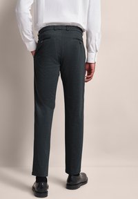 Dunkelgraue Hose aus strukturiertem Stoff, Slim Fit, mit zwei Gesäßtaschen, kombiniert mit einem weißen Hemd und schwarzen Schuhen.