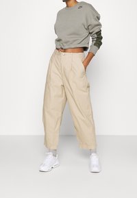 Grå kortad sweatshirt med gröna accenter och en logotyp. Beiga vida byxor med sidofickor. Vita sneakers med texturerad detalj.