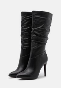 Botines de cuero negro con un diseño holgado, punteras puntiagudas y tacones de aguja. Textura suave con sutiles acentos plegados.
