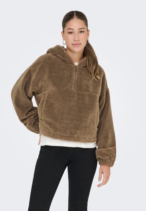 Sudadera de forro polar marrón con cierre de media cremallera, puños acanalados y un corte relajado. Tejido suave y texturizado con un brillo sutil. Lleva una camiseta blanca debajo.