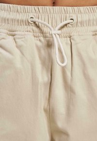 Pantaloni scurți din bumbac bej, având un talie elastică, închidere cu șnur și o textură moale. Vedere detaliată care arată clar țesătura și orificiile.