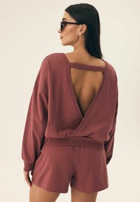 Oversized sweter w kolorze rdzy z otwartym plecami, w połączeniu z pasującymi szortami. Miękka dzianina z luźnym krojem.