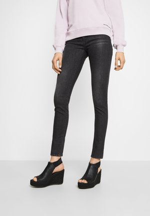Sorte skinny jeans med en mørk vask, parret med åbne sorte wedge-sandaler med en tekstureret overflade og et slingback-design.
