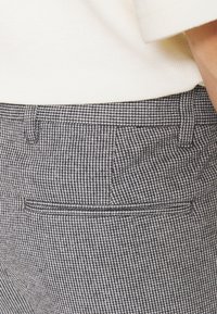 Spodnie w kratę houndstooth w czerni i bieli, z bocznymi kieszeniami, dopasowanym krojem i gładką fakturą materiału, cięte do poziomu talii.