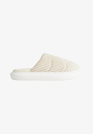 Chaussons matelassés beige avec une tige en tissu doux, semelle blanche moulée et design facile à enfiler, présentant des lignes horizontales surélevées pour une texture.