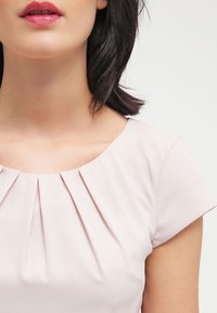 Robe rose pâle avec un col plissé, des manches courtes et une texture lisse. Design subtil sans motifs ni accents supplémentaires.