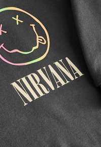 Schwarzer Hoodie mit einem mehrfarbigen Smiley-Gesicht-Logo und dem Schriftzug "NIRVANA" in fetter Creme-Schrift. Weicher, strukturierter Stoff.