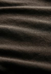 Primer plano de tela suave de color marrón oscuro con pliegues sutiles y una superficie ligeramente texturizada.