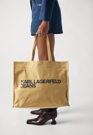 Sac en toile de coton jaune avec "KARL LAGERFELD JEANS" en lettres noires en gras. Poignées renforcées, forme rectangulaire et texture lisse.